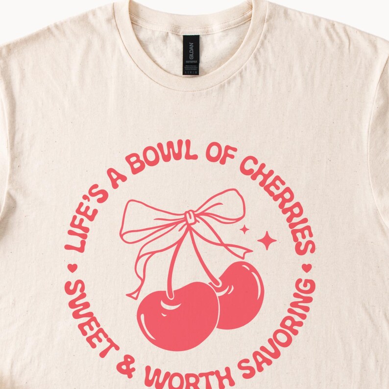 May include: A cream colored t-shirt with a pink graphic that says "Life's a bowl of cherries - sweet & worth savoring". The graphic features a cherry with a bow on top.