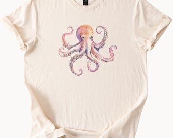 May include: A cream-coloured t-shirt with a watercolour octopus design. The octopus is rendered in pink, purple, and orange hues, with detailed tentacles and a central body. The shirt has a classic crew neck and short sleeves.