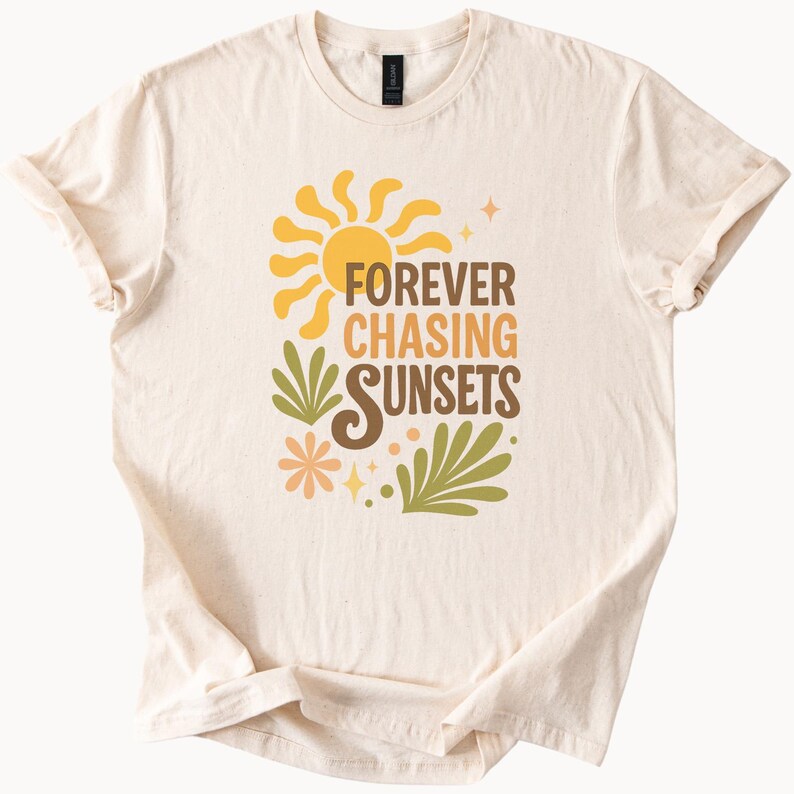 May include: Cream-colored t-shirt featuring a retro design with a yellow sun, green leaves, and the text "FOREVER CHASING SUNSETS" in brown and orange. The shirt has short sleeves and a crew neck.