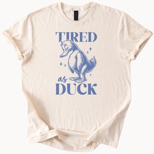 Camiseta "Cansado como un pato", divertida camiseta gráfica de pájaro exhausto, color beige natural, algodón, unisex.