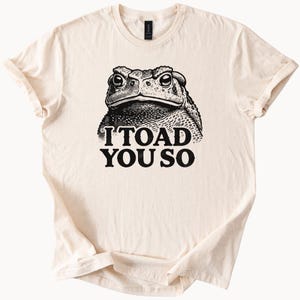May include: A beige t-shirt with a black and white illustration of a toad and the text "I TOAD YOU SO".
