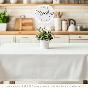 Puede incluir: Un mantel blanco cubre una mesa, con una pequeña planta en maceta en el centro. El texto "FULLY Mockup EDITABLE" está en un círculo encima de la planta. El fondo muestra una cocina con gabinetes blancos y estantes de madera.