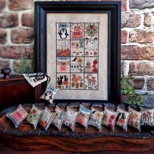 Peut inclure: Douze petits coussins carrés en tissu avec des images brodées d'animaux et de plantes représentant chaque mois de l'année. Les coussins sont disposés en rangée sur une surface en bois. Les coussins sont de différentes couleurs, notamment le rouge, le vert, le bleu, le jaune et le marron.