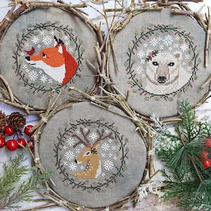 May include: Three round cross-stitch embroidery hoops with winter animal designs. The hoops are made of natural twigs and feature a fox, a polar bear, and a reindeer.