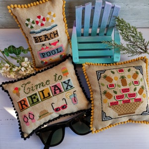 Può includere: Tre fodere per cuscini ricamate con un tema estivo da spiaggia. I cuscini sono beige con bordino giallo e presentano ricami colorati di motivi a tema spiaggia. Un cuscino dice "Beach Pool", un altro dice "Time to Relax" e il terzo ha un cesto di frutta e anguria.