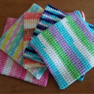 May include: Five crocheted dishcloths in various colours, including pink, green, blue, and white. The dishcloths are stacked on top of each other.
