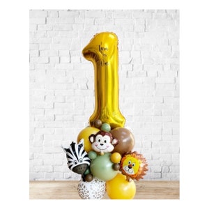 May include: A gold number one balloon with the text "Tara is One" on it. The balloon is surrounded by smaller balloons with animal faces, including a zebra, monkey, and lion.