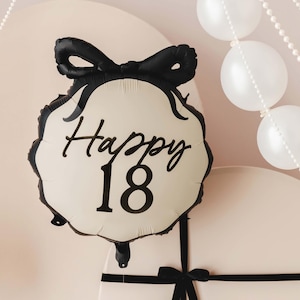 K&ouml;nnte beinhalten: Ein wei&szlig;er Ballon mit schwarzer Aufschrift "Happy 18" und einer schwarzen Schleife. Der Ballon h&auml;ngt an einer wei&szlig;en Decke mit einer Schnur aus wei&szlig;en Perlen.