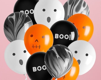 May include: A collection of Halloween-themed balloons in black, white, and orange. Some balloons have ghost faces, skull faces, or the word "BOO!" printed on them. Others have a marbled design. The balloons are arranged against a pink background.