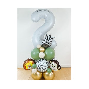 May include: A gray number two balloon with the text "Chris is two" on it. The balloon is surrounded by green, gold, and white balloons with animal faces, including a zebra, a lion, and a monkey.