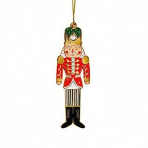 Könnte beinhalten: Ein roter und goldener Nussknacker-Anhänger mit grünem Hut und einem weiß-schwarz gestreiften Uniform. Der Anhänger hat eine goldene Schnur zum Aufhängen.