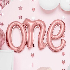 Può includere: Una ghirlanda di palloncini rosa e grigi con palloncini in lamina oro rosa che compongono la parola "uno" per una festa di primo compleanno.