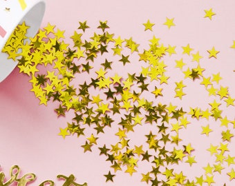 May include: A pink background with gold star confetti spilling out of a colorful striped paper cup. The word "sweet" is written in gold script on the pink surface.