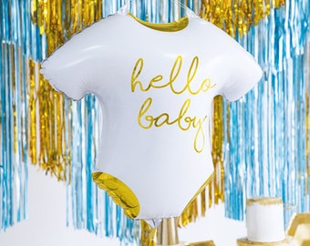 Può includere: Pallone bianco a forma di body con il testo "hello baby" in lettere dorate. Il pallone è appeso davanti a una tenda di alluminio blu e oro.