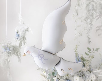 以下が含まれることがあります： 白い鳩の形をした風船で、薄い青のリボンと金のアクセントが付いています。風船は白い背景に白い花が飾られています。