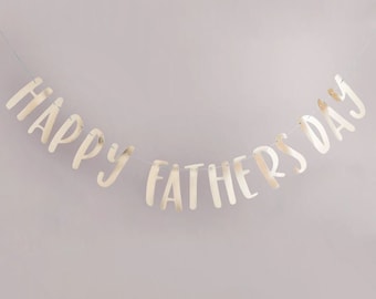 Puede incluir: Bandera de papel de aluminio dorado con el texto "Happy Father's Day" colgada sobre un fondo rosa claro.