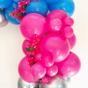 May include: A vibrant balloon arrangement featuring blue, pink, and silver balloons. Pink flowers are interspersed throughout the arrangement. The balloons vary in size, creating a dynamic and festive display.