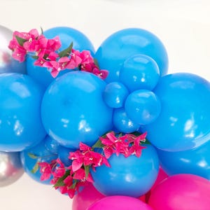 May include: A cluster of blue, silver, and pink balloons, adorned with bright pink flowers. The balloons vary in size, creating a dynamic and festive arrangement. Ideal for party decorations.