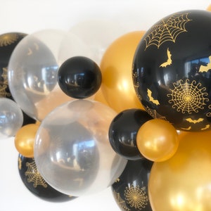 Op de afbeelding: Een verzameling zwarte en gouden ballonnen met spinnenweb- en vleermuisontwerpen. De ballonnen zijn in een cluster gerangschikt, waardoor een feestelijke en spookachtige sfeer ontstaat.