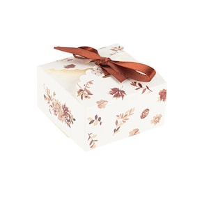 May include: A small white gift box with a brown ribbon and a floral pattern. The box is decorated with a variety of leaves and flowers in shades of brown and orange.