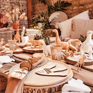 May include: A dinosaur-themed table setting with planters, cups, and figurines. Wooden coasters and place settings are also present. The colour scheme is beige, brown, and white, creating a rustic aesthetic. The planters and cups are designed with dinosaur silhouettes.
