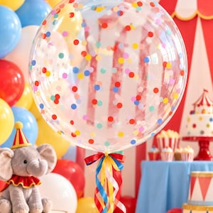 May include: A large, clear, spherical balloon filled with colorful confetti dots in shades of red, blue, yellow, and pink. The balloon is tied with a cluster of long, curling ribbons in red, blue, yellow, and pink, hanging down from the base.