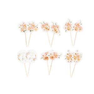 Op de afbeelding: Een verzameling bloemen cupcake toppers met houten stokjes. De toppers hebben bloemen in aquarel-stijl in perzik- en crèmekleur. Sommige toppers hebben de tekst "Bride to Be" in gouden letters. Perfect voor een bruidsfeest of bruiloft.