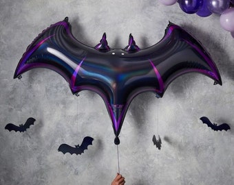 May include: A large iridescent black bat-shaped balloon with purple accents. The balloon is hanging from the ceiling with smaller black bat cutouts hanging from it.
