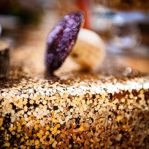 May include: A close-up of a gold glitter surface with a purple leaf-shaped object on top.