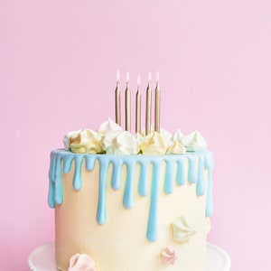 K&ouml;nnte beinhalten: Ein wei&szlig;er Kuchen mit blauer Zuckerglasur und wei&szlig;en Baiser-Dekorationen. F&uuml;nf silberne Kerzen brennen auf dem Kuchen.