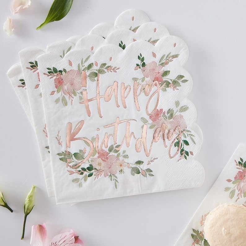 May include: White scalloped-edge paper napkins with a floral design and the words "Happy Birthday" in rose gold script. The napkins feature pink flowers and green leaves, perfect for a birthday celebration.