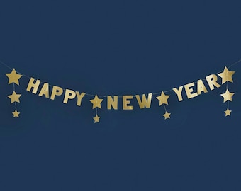 May include: Gold foil banner with the words "HAPPY NEW YEAR" and star-shaped cutouts. The banner is strung on a thin string and hangs against a dark blue background. Festive decoration for New Year's celebrations.
