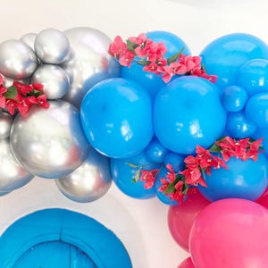 May include: A festive balloon arch featuring silver, blue, and pink balloons, adorned with red flowers. The balloons are arranged in a curved shape, creating a celebratory and decorative display, perfect for parties and events.