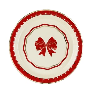 Puede incluir: Un plato de papel redondo con un centro de color crema y una ilustración de un lazo rojo. El plato tiene un borde interior festoneado en rojo y dorado, y un borde exterior ancho de color rojo decorado con puntos blancos y detalles dorados.