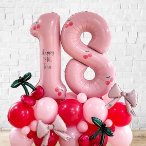 Könnte beinhalten: Eine festliche Ballongirlande zum 18. Geburtstag. Die Dekoration besteht aus großen, rosafarbenen Zahlenballons, die mit Kirschen verziert sind, sowie einer Basis aus roten und rosa Ballons. Auf dem Ballon mit der Nummer 1 steht der Text "Happy 18th. Tara".