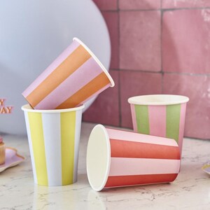 May include: Four striped paper cups in different color combinations. The cups are pink, orange, yellow, and red with white stripes.