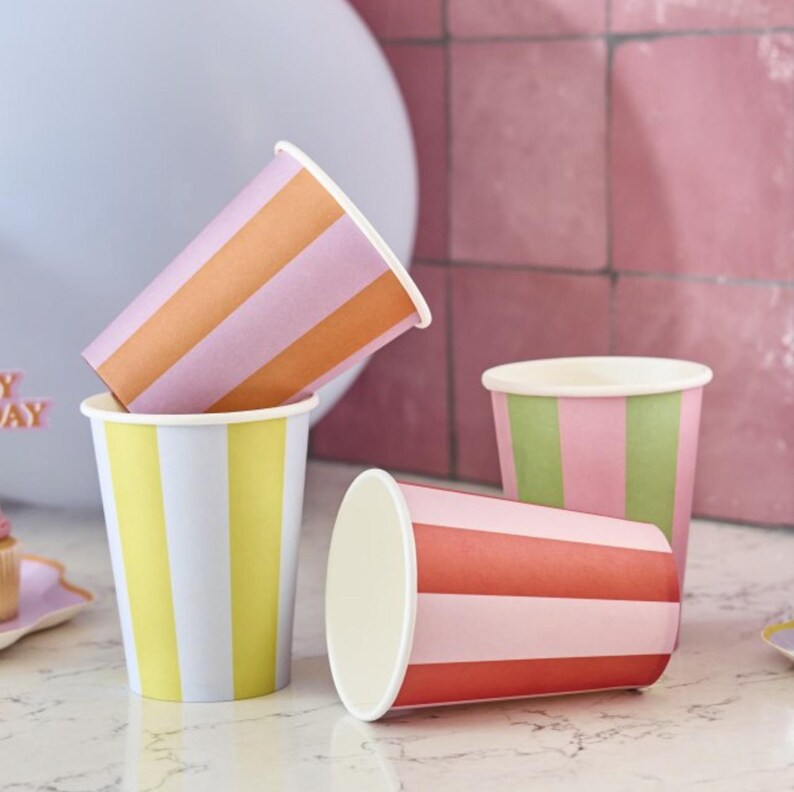 May include: Four striped paper cups in different color combinations. The cups are pink, orange, yellow, and red with white stripes.