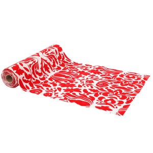 May include: A rolled-up table runner with a red and white floral pattern. The runner is unrolled, showing a repeating design of stylized flowers and leaves. The colour scheme is bright red against a white background.