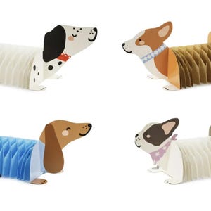 Puede incluir: Cuatro decoraciones de perros de papel en varias razas. Uno es blanco con manchas negras, otro es marr&oacute;n y blanco, un tercero es marr&oacute;n y azul, y el &uacute;ltimo es blanco con acentos negros y rosas. Cada perro tiene un cuerpo de panal.