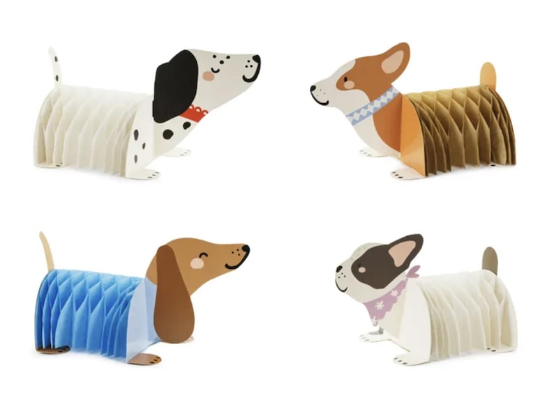 Puede incluir: Cuatro decoraciones de perros de papel en varias razas. Uno es blanco con manchas negras, otro es marr&oacute;n y blanco, un tercero es marr&oacute;n y azul, y el &uacute;ltimo es blanco con acentos negros y rosas. Cada perro tiene un cuerpo de panal.