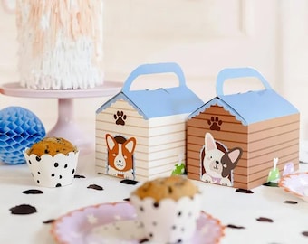 May include: Two dog-themed treat boxes, one blue and one brown, with a dog peeking out of each. The boxes are on a table with a cupcake in front of each.