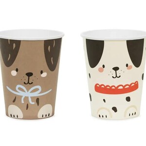 Puede incluir: Dos vasos de papel con ilustraciones de perros. Un vaso presenta un perro marr&oacute;n con una pajarita azul y el otro vaso presenta un d&aacute;lmata blanco y negro con un collar rojo.
