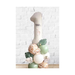 May include: A beige number one balloon with the name "TARA" and a giraffe illustration. The balloon is part of a balloon arrangement with safari-themed balloons in white, green, and giraffe print, and animal cutouts.