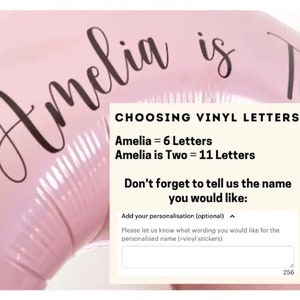 May include: Pink balloon with the text "Amelia is Two" in black cursive lettering. A white box with the text "CHOOSING VINYL LETTERS" and instructions for customizing the balloon with vinyl letters.