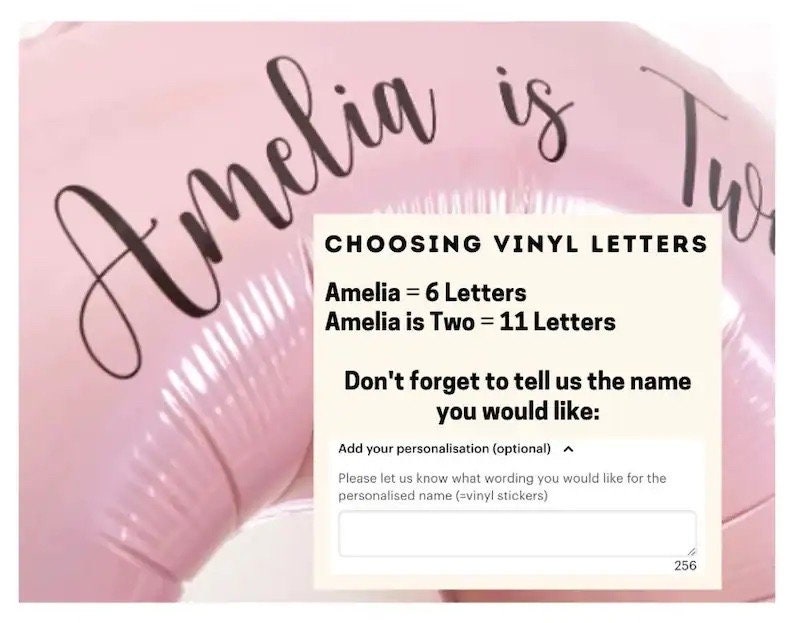 May include: Pink balloon with the text "Amelia is Two" in black cursive lettering. A white box with the text "CHOOSING VINYL LETTERS" and instructions for customizing the balloon with vinyl letters.
