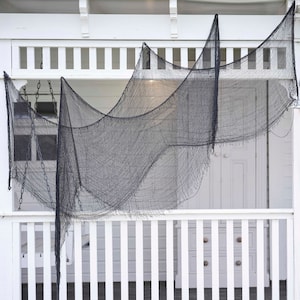 May include: Black, tattered fabric draped over a white porch railing and ceiling. The fabric is hung in a wavy pattern, creating a spooky, Halloween-themed decoration. The porch has a white railing and a white door.