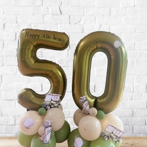 May include: A gold foil balloon display forming the number "50", with the inscription "Happy 50th Tara". The balloons are adorned with golf-themed decorations, such as golf carts and golf balls, and are set on a base of green and cream balloons.