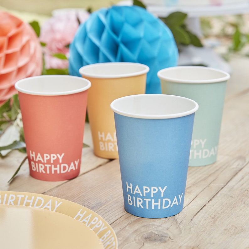 May include: Four paper cups with a gradient color design. The cups are blue, yellow, green, and orange. Each cup has the text "Happy Birthday" printed on the front.