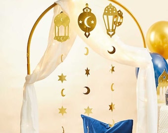 May include: Gold Ramadan decorations hanging from a white canopy. The decorations include stars, crescent moons, and lanterns.