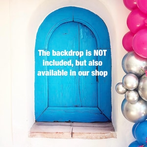 May include: A bright blue arched door set in a white wall, framed by pink, silver, and blue balloons. The text on the door reads: "The backdrop is NOT included, but also available in our shop."
